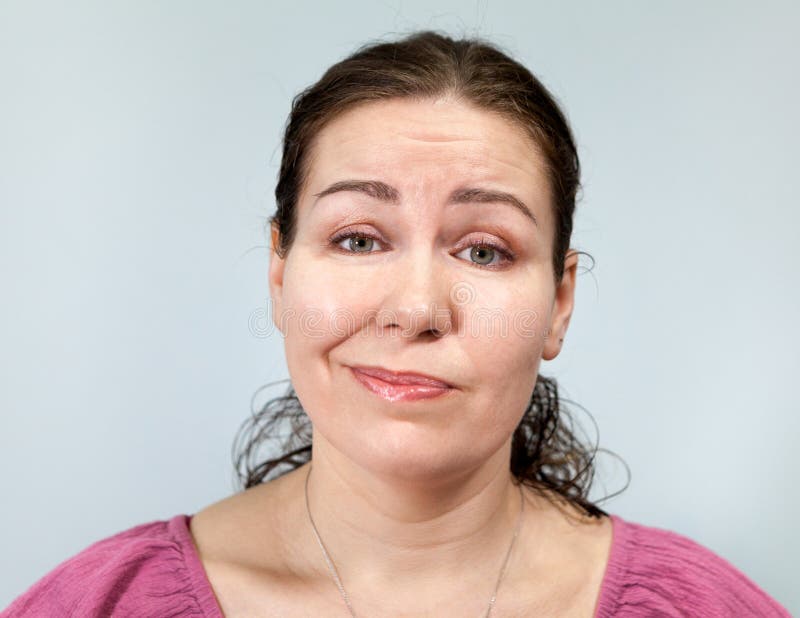 Erwachsene Frau mit einem Grinsen auf dem Gesicht, Portrait auf grauem Hintergrund, Emotionsreihe stockfoto