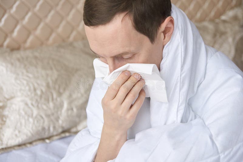 Erwachsene kaukasische Männer mit Erkältung oder Allergien, die im Schlafzimmer Nase in Gewebe blasen lizenzfreies stockfoto