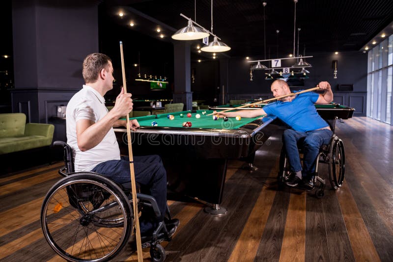 Erwachsene Männer mit Behinderung im Rollstuhl spielen Billard im Club lizenzfreies stockbild