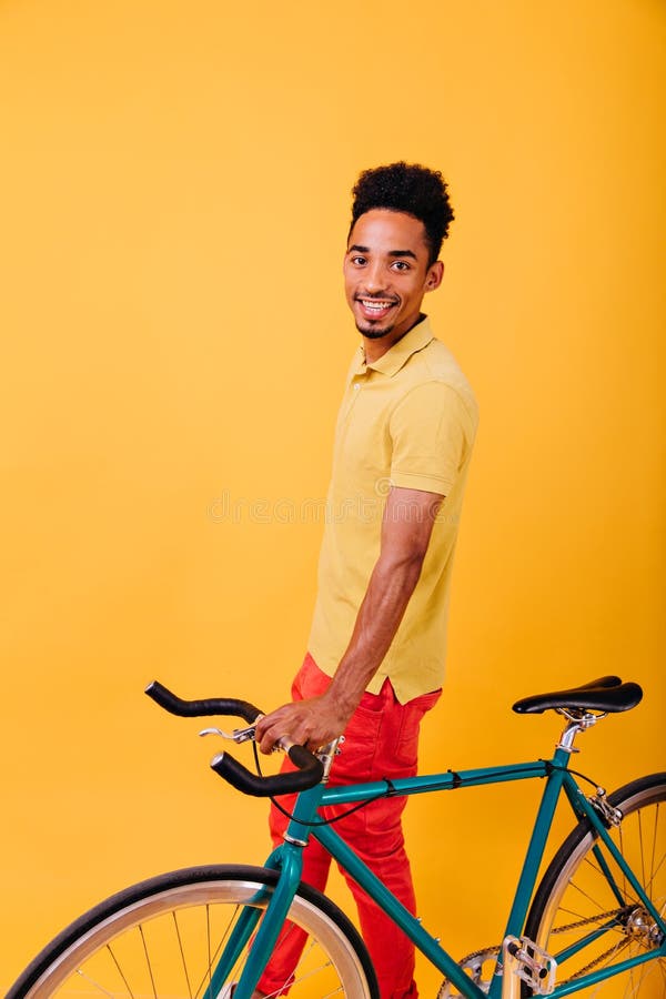 Esaltato uomo africano in abiti eleganti con una bicicletta verde. foto in interni di un ragazzo di colore sorridente fotografia stock