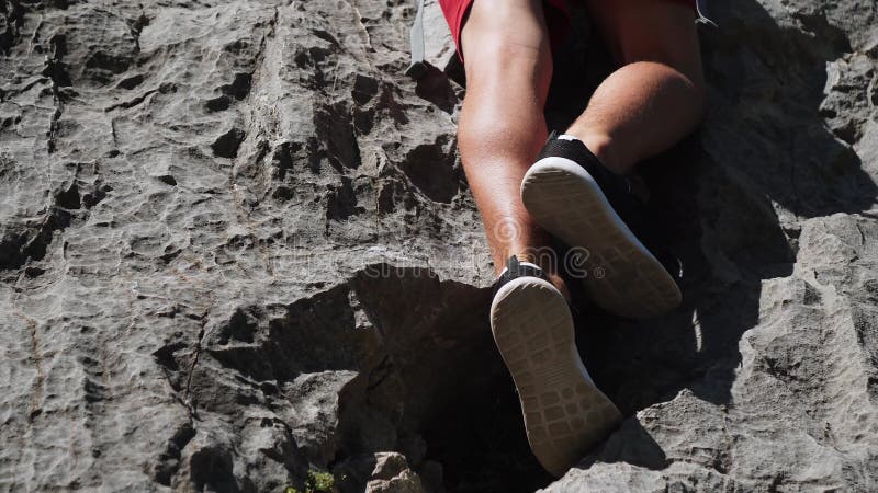 Escalada rochosa no verão. pernas de homem escalador dificilmente funcionam para subir para o topo.