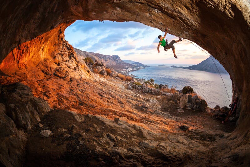 Escalador de roca masculino que sube a lo largo de un tejado en una cueva