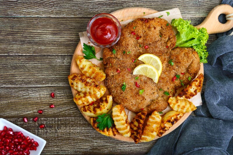 Escalope grande con las patatas de oro cocidas en una tabla de cortar de madera Schnitzel de salchicha de Francfort fotografía de archivo Escalope grande con las patatas de oro cocidas en una tabla de cortar de madera Schnitzel de salchicha de Francfort fotografía de archivo
