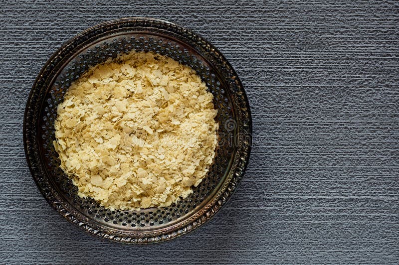 Top view of dried nutritional yeast flakes on a vintage metal plate on a gray, textured background. Top view of dried nutritional yeast flakes on a vintage metal plate on a gray, textured background