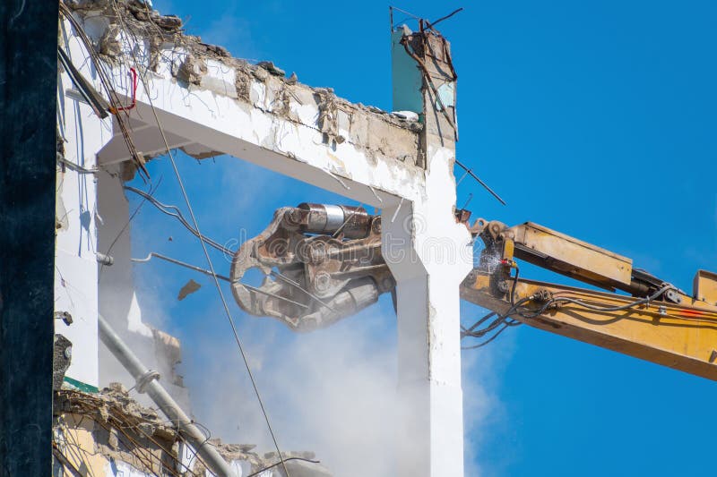 Escavador demolindo estrutura do edifício contra o céu azul fotografia de stock