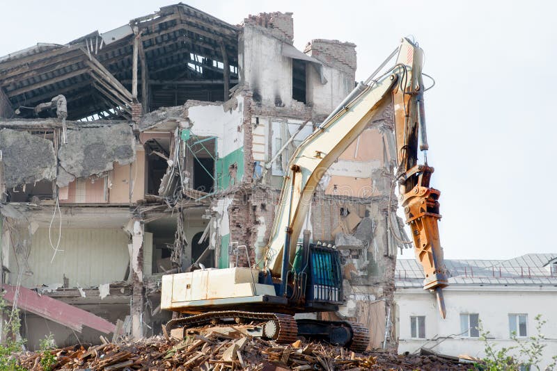 Escavador demolindo um edifício de tijolos Edifício de demolição de máquinas imagem de stock