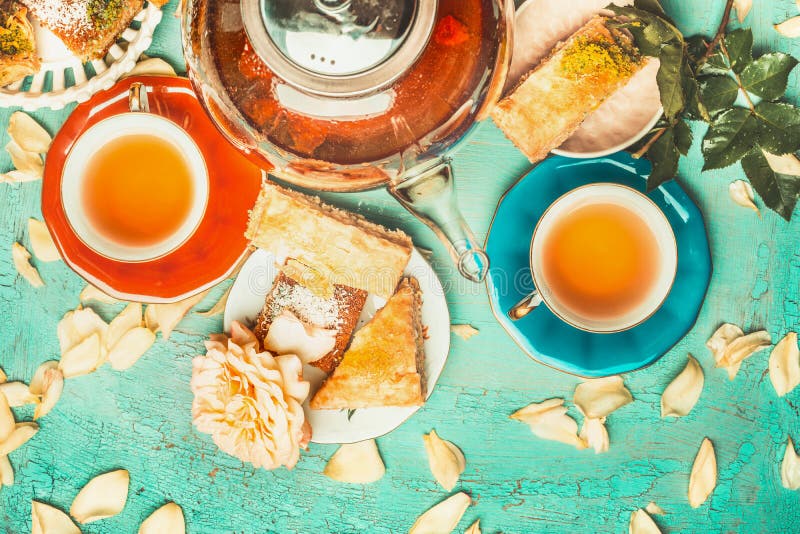 Nice tea brunch scene with colorful cup of tea, tea pot , cakes and flowers on turquoise shabby chic background, top view. Nice tea brunch scene with colorful cup of tea, tea pot , cakes and flowers on turquoise shabby chic background, top view