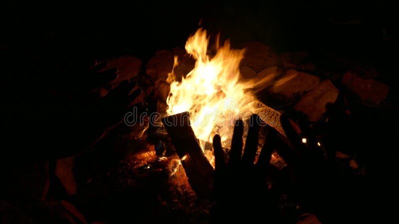 Escena de fogatas con silueta de mano humana calentando por fuego