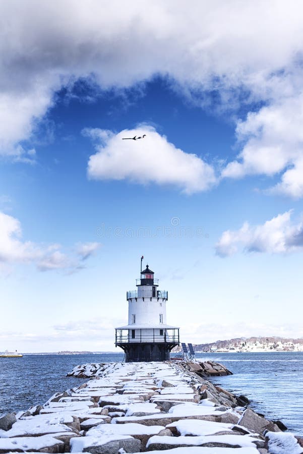 A jetty leading to the Spring Point Ledge Lighthouse in South Portland Maine on a blue sky winter day as a jet flies above in new england. A jetty leading to the Spring Point Ledge Lighthouse in South Portland Maine on a blue sky winter day as a jet flies above in new england.