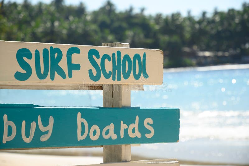 Surf school and lessons sign on tropical beach with big wave. Surf school and lessons sign on tropical beach with big wave.