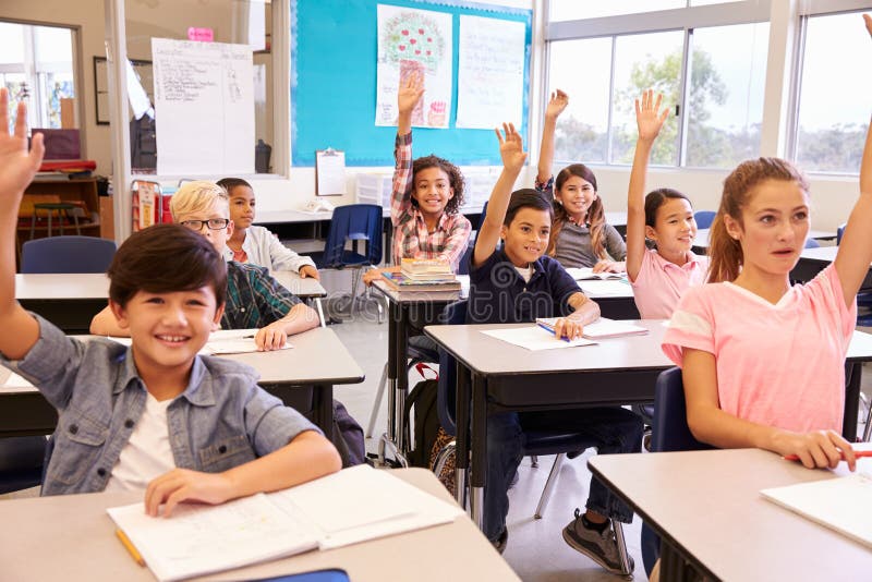 A escola primária caçoa em uma sala de aula que levanta suas mãos