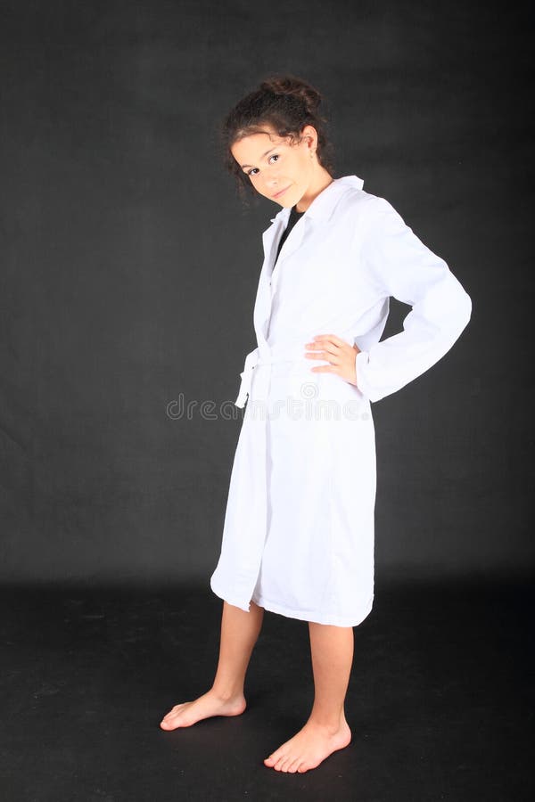 Teenage girl - barefoot schoolkid with brunette hair dressed in white lab coat on black background. Doctor and medicine concept. Teenage girl - barefoot schoolkid with brunette hair dressed in white lab coat on black background. Doctor and medicine concept.