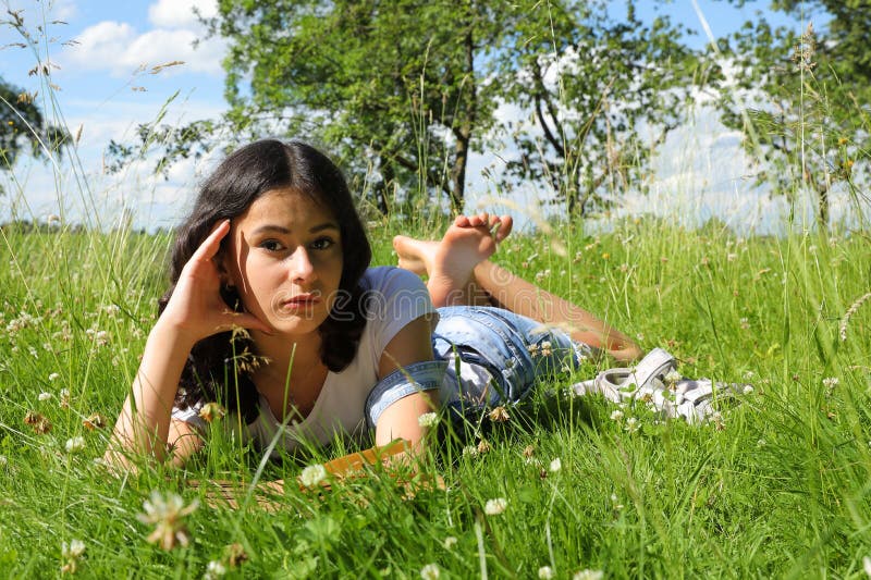 Teenage girl - barefoot schoolkid with brunette hair lying in grass. Portrait photography concept. Teenage girl - barefoot schoolkid with brunette hair lying in grass. Portrait photography concept.