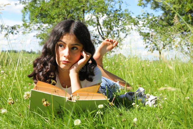 Teenage girl - smart schoolkid with brunette hair lying in grass and reading an old book. School and education concept. Teenage girl - smart schoolkid with brunette hair lying in grass and reading an old book. School and education concept.