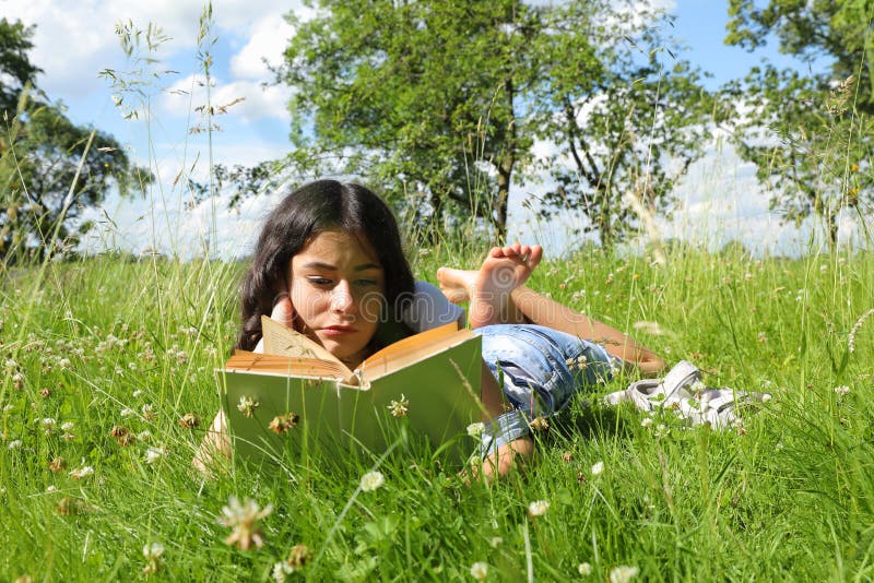 Teenage girl - smart schoolkid with brunette hair lying in grass and reading an old book. School and education concept. Teenage girl - smart schoolkid with brunette hair lying in grass and reading an old book. School and education concept.