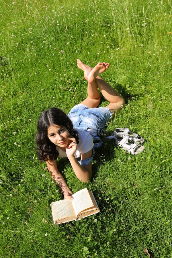 Teenage girl - smart schoolkid with brunette hair lying in grass and reading an old book. School and education concept. Teenage girl - smart schoolkid with brunette hair lying in grass and reading an old book. School and education concept.