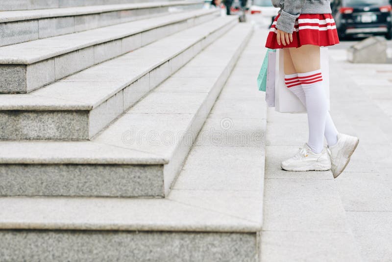 Cropped image of schoolgirl in short skirt and thigh high socks walking up the stairs with shopping bags in hands. Cropped image of schoolgirl in short skirt and thigh high socks walking up the stairs with shopping bags in hands