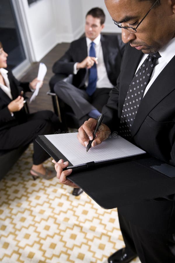 Escrita do homem de negócios do americano africano no bloco de notas fotografia de stock Escrita do homem de negócios do americano africano no bloco de notas fotografia de stock
