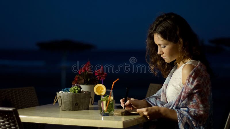 Escritor de sexo femenino inspirado que hace notas en el cuaderno, trabajando en historia de amor romántica imagen de archivo Escritor de sexo femenino inspirado que hace notas en el cuaderno, trabajando en historia de amor romántica imagen de archivo