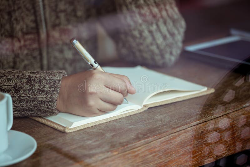 Escritura de la mano de la mujer en el cuaderno en el café en día lluvioso