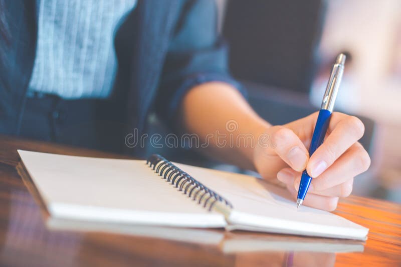 Escritura de la mujer de negocios en un notebookwith una pluma en la oficina. Escritura de la mujer de negocios en un cuaderno con una pluma en la oficina