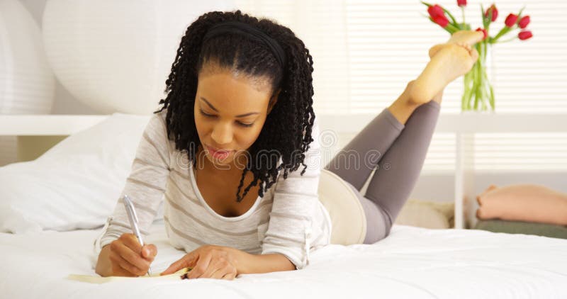 Escritura joven de la mujer negra en diario fotos de archivo libres de regalías Escritura joven de la mujer negra en diario fotos de archivo libres de regalías