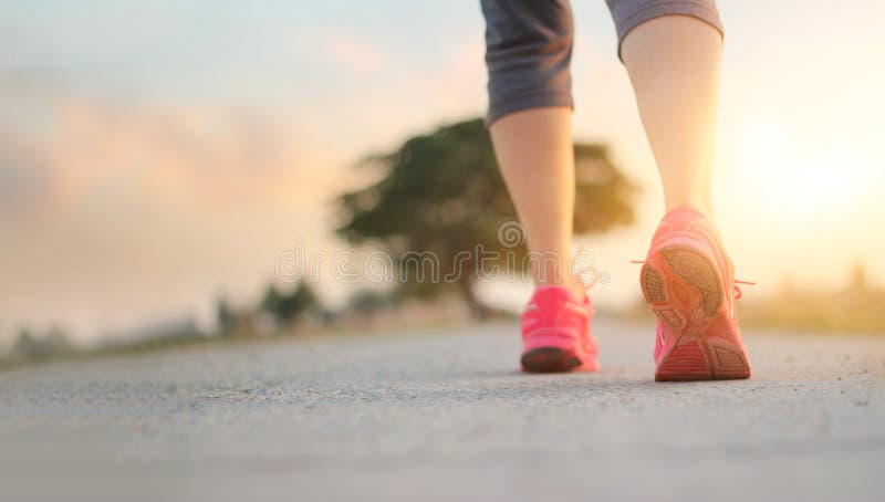 Esercizio di camminata della donna dell'atleta sulla strada rurale nel backgroun di tramonto