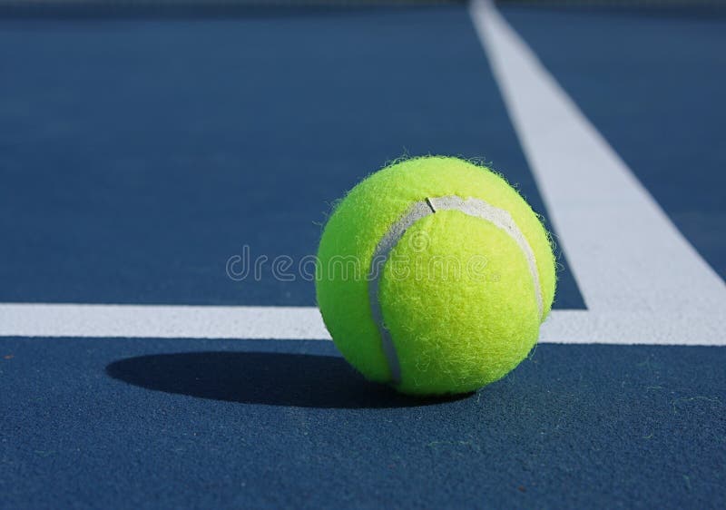 Yellow tennis ball at the baseline of a blue court. Yellow tennis ball at the baseline of a blue court