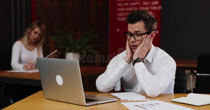 Esforço no trabalho O homem de negócios novo olha o trabalho muito cansado no escritório com portátil Negócio, pessoa, documento