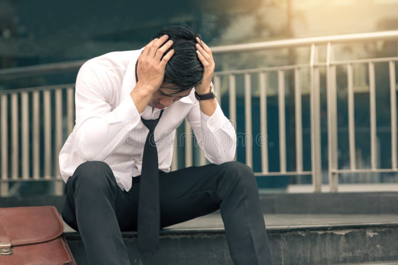 Esforço novo asiático do homem de negócios que senta-se no escritório principal com suas mãos que cobrem sua cabeça contra fotografia de stock royalty free Esforço novo asiático do homem de negócios que senta-se no escritório principal com suas mãos que cobrem sua cabeça contra fotografia de stock royalty free