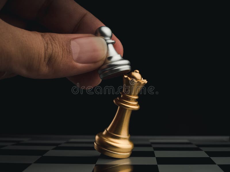 A peça de xadrez da rainha de ouro em pé com peças de xadrez de peão de  prata caindo no tabuleiro de xadrez em fundo escuro com espaço de cópia.  liderança, vencedor