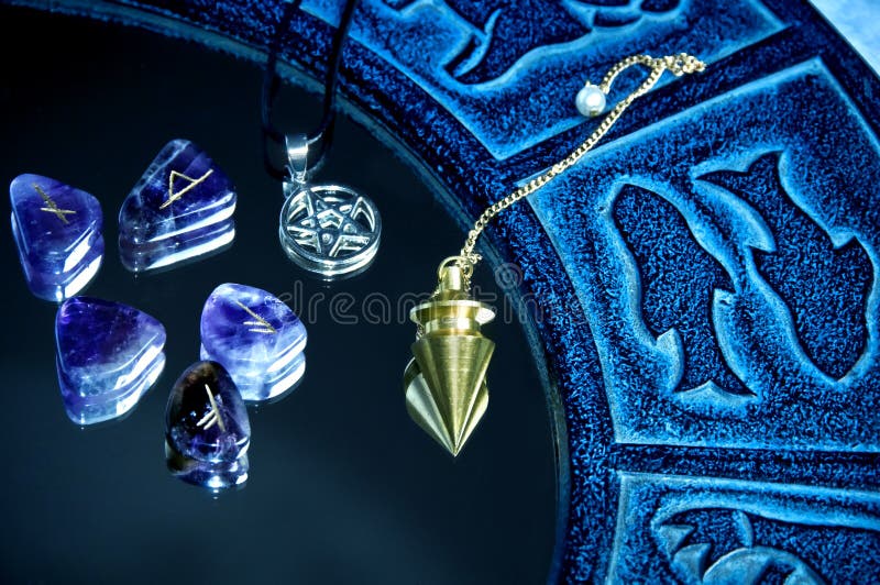 Esoteric tools pentagram, runes, pendulum on mirror surface with blue zodiac