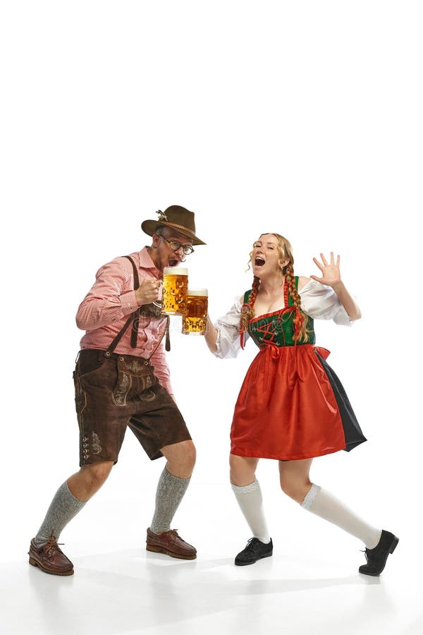 Two celebrating friends. Shouting man and woman wearing traditional German outfits, having clinking glasses with Bavarian beer. Concept of alcohol, traditions, holidays, festival. Copy space for ad. Two celebrating friends. Shouting man and woman wearing traditional German outfits, having clinking glasses with Bavarian beer. Concept of alcohol, traditions, holidays, festival. Copy space for ad