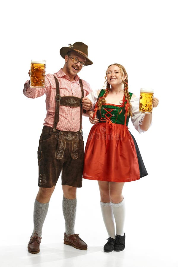 Two celebrating friends. Full lenght portrait of smiling man and woman wearing folk festival outfits, with Bavarian beer glasses. Concept of alcohol, traditions, holidays, festival. Copy space for ad. Two celebrating friends. Full lenght portrait of smiling man and woman wearing folk festival outfits, with Bavarian beer glasses. Concept of alcohol, traditions, holidays, festival. Copy space for ad