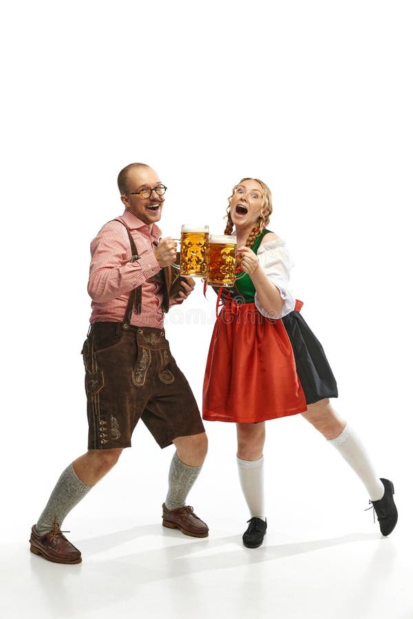 Two cheerful friends. Full lenght portrait of emotional man and woman wearing folk festival outfits with Bavarian beer glasses. Concept of alcohol, traditions, holidays, festival. Copy space for ad. Two cheerful friends. Full lenght portrait of emotional man and woman wearing folk festival outfits with Bavarian beer glasses. Concept of alcohol, traditions, holidays, festival. Copy space for ad