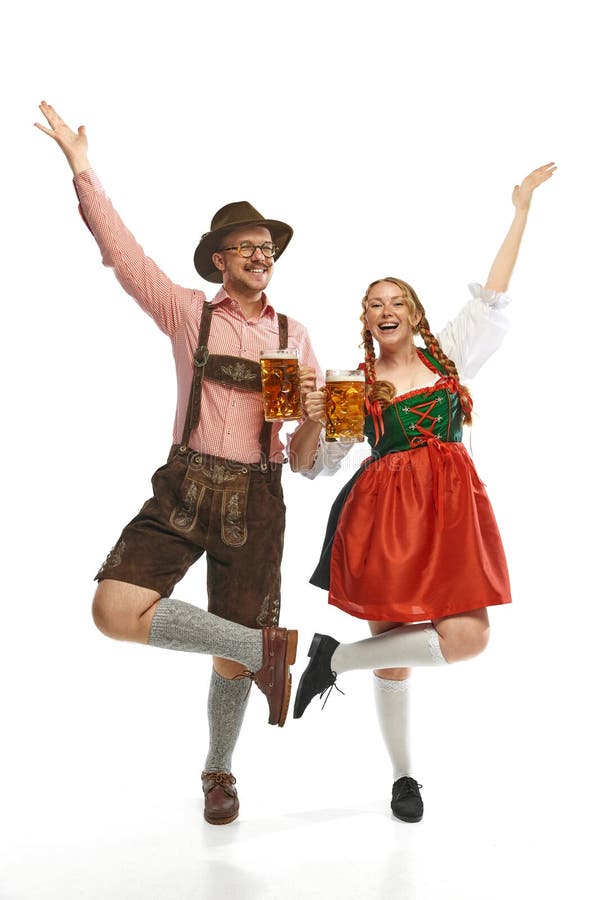 Two dancing friends. Full lenght portrait of emotional man and woman wearing folk festival outfits with Bavarian beer glasses. Concept of alcohol, traditions, holidays, festival. Copy space for ad. Two dancing friends. Full lenght portrait of emotional man and woman wearing folk festival outfits with Bavarian beer glasses. Concept of alcohol, traditions, holidays, festival. Copy space for ad
