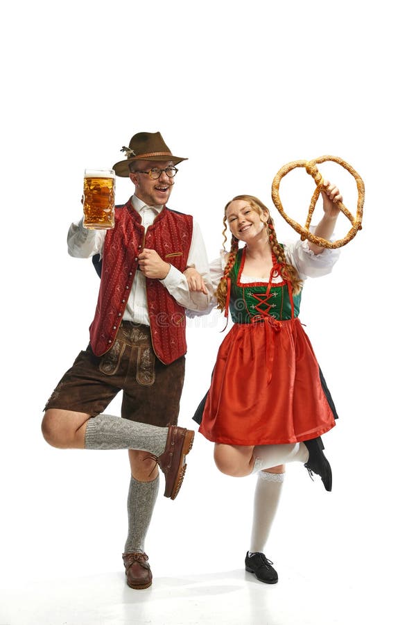 Full lenght portrait of emotional man and woman wearing folk festival outfits with Bavarian beer glasses and huge pretzel. Concept of alcohol, traditions, holidays, festival. Copy space for ad. Full lenght portrait of emotional man and woman wearing folk festival outfits with Bavarian beer glasses and huge pretzel. Concept of alcohol, traditions, holidays, festival. Copy space for ad