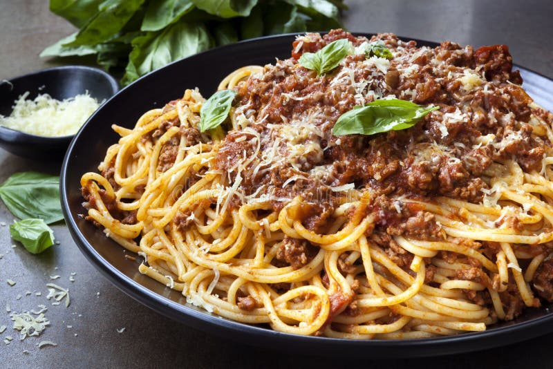 Spaghetti bolognese in black serving platter, with fresh basil and parmesan. Spaghetti bolognese in black serving platter, with fresh basil and parmesan.