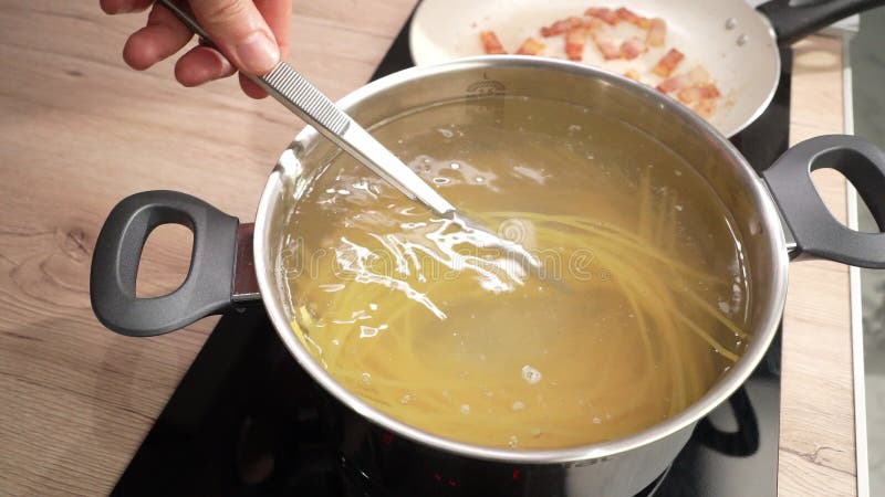 Espagueti se comprueba si está preparado en una olla de agua hirviendo con pinzas.