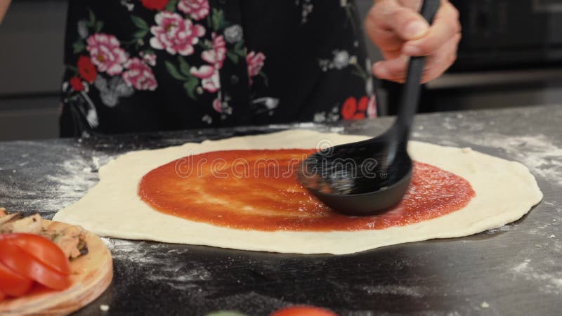 Esparcir salsa de tomate en base de pizza. chef hembra vertiendo salsa en pizza con salsa. proceso de elaboración de pizza. cocció metrajes
