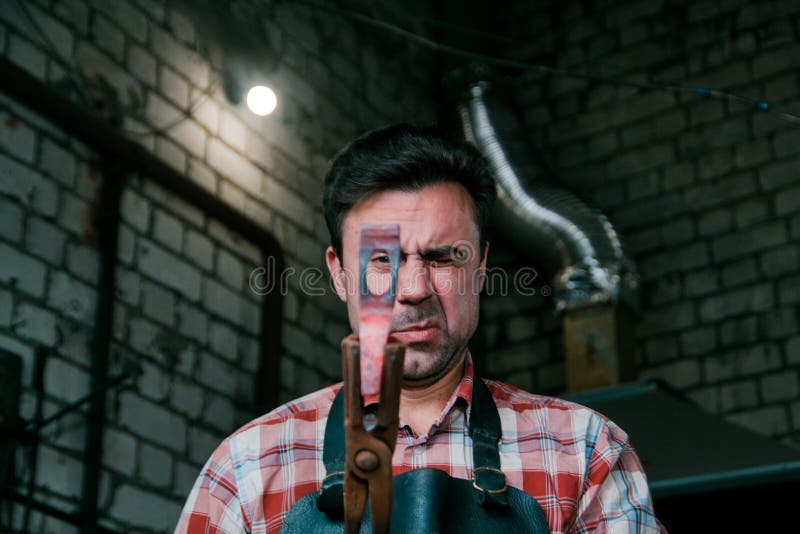 Espaço de trabalho do ferreiro Ferreiro que trabalha com o workpiece encarnado do metal do martelo novo no batente em uma forja V fotos de stock Espaço de trabalho do ferreiro Ferreiro que trabalha com o workpiece encarnado do metal do martelo novo no batente em uma forja V fotos de stock