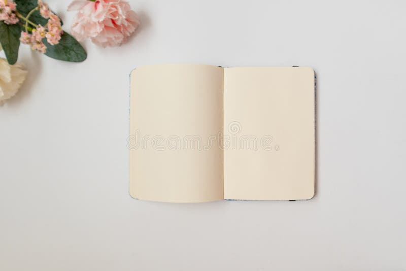 Espaço de trabalho mínimo notebook em branco com flores em fundo branco. espaço de cópia plano visão superior