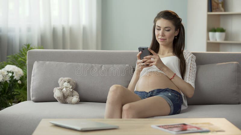 Esperando a mulher na mensagem de datilografia do sofá no telefone celular, trabalhos em rede sociais