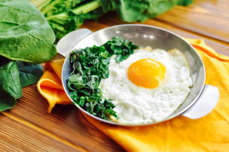 Espinaca cocida verde con huevo frito en placa de hierro de la sartén. huevos fritos desayuno saludable sobre fondo de mesa de mad