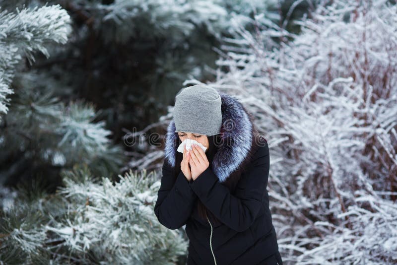 Espirrar fêmea A jovem mulher bonita tem a gripe e a febre no dia de inverno exterior foto de stock Espirrar fêmea A jovem mulher bonita tem a gripe e a febre no dia de inverno exterior foto de stock