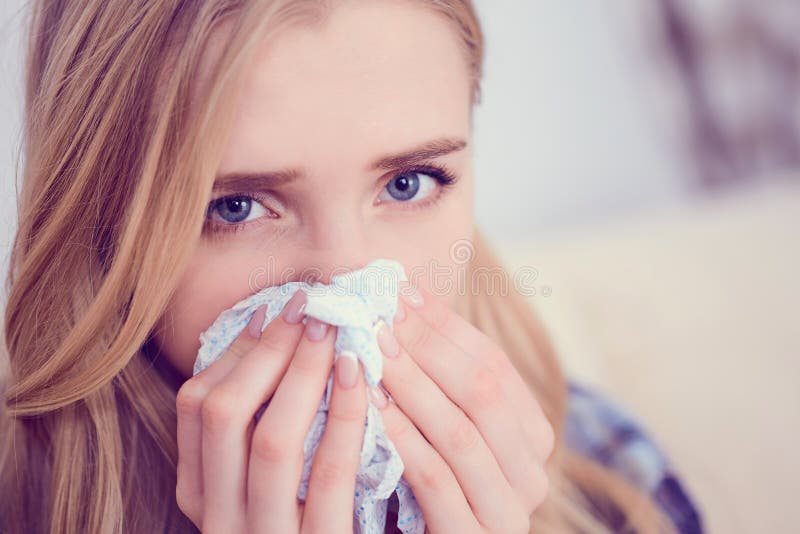 Espirro caucasiano doente novo da mulher em casa no sofá com um frio Lenço de papel usado menina que funde seu nariz Médico e