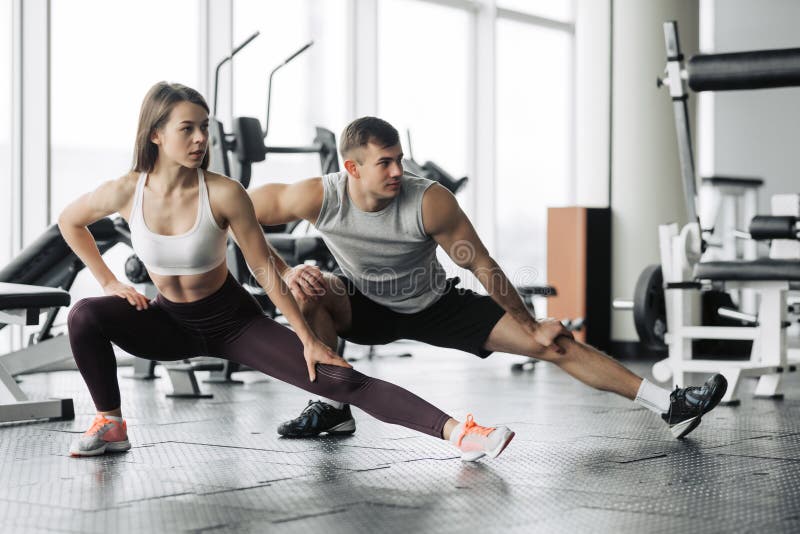 Esporte, aptidão, estilo de vida e conceito dos povos - homem e mulher de sorriso que esticam no gym Esporte, aptidão, estilo de vida e conceito dos povos - homem e mulher de sorriso que esticam no gym
