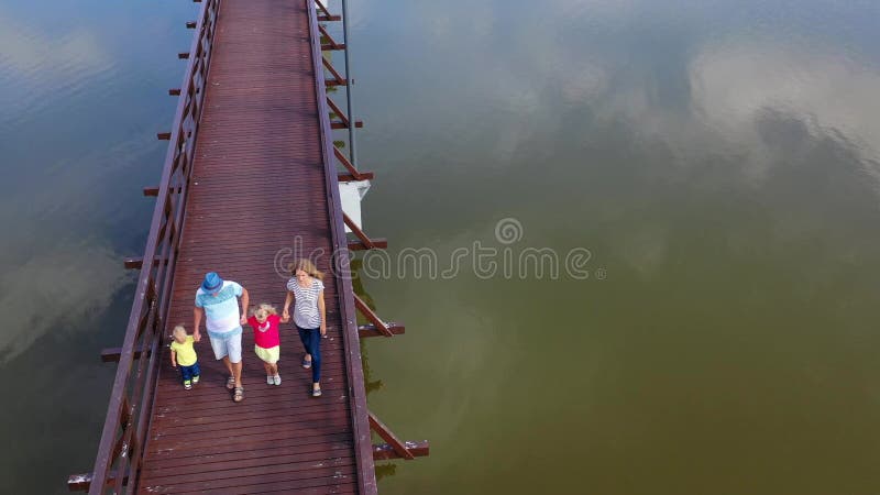 Esposa com marido e seus filhos andando na ponte de madeira segurando as mãos