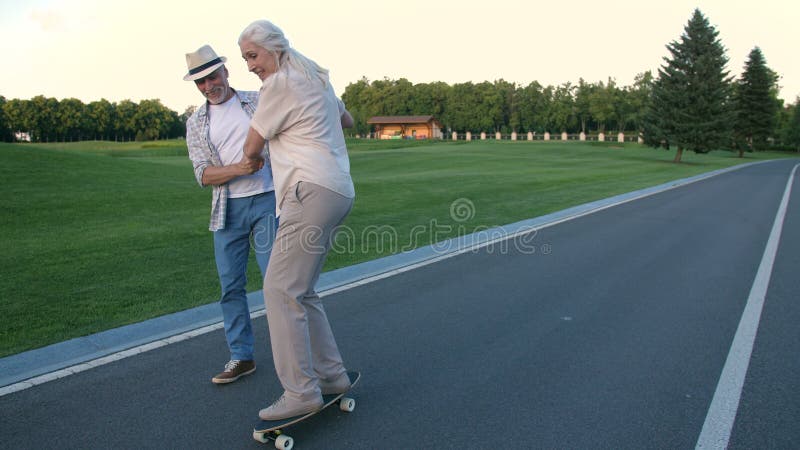 Esposa de ensino do marido ao skate no parque do verão