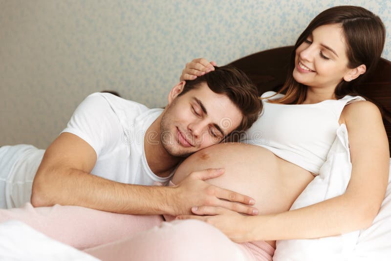 Esposa embarazada joven sonriente que miente en cama con su marido imagen de archivo libre de regalías Esposa embarazada joven sonriente que miente en cama con su marido imagen de archivo libre de regalías